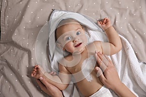 Mother applying moisturizing cream onto her little baby`s skin on bed, closeup