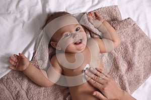 Mother applying moisturizing cream onto her little baby`s skin on towel