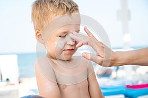 Mother applying sunscreen protection creme on cute little baby boy kid face. Mum using sunblocking lotion to protect son