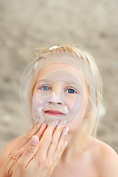 Mother applying sunscreen protection creme on cute little daughter face. Mom using sunblocking lotion to protect kid girl from sun