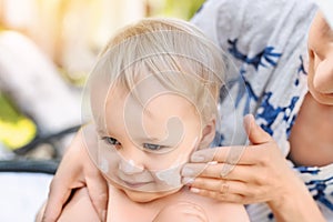 Mother applying sunscreen protection creme on cute little toddler boy face. Mom using sunblocking lotion to protect baby