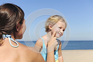 Mother applying suntan lotion to her daughter photo