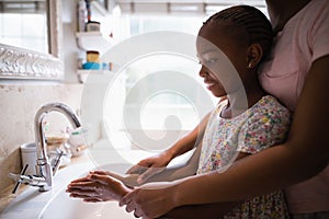 Mother assisting daughter while washing hands at bathroom sink