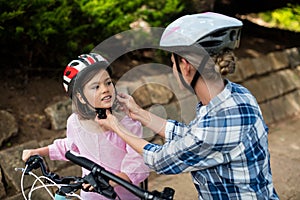 Mother assisting daughter in wearing bicycle helmet in park