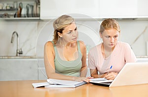 Mother assisting teenage daughter doing school assignment at home