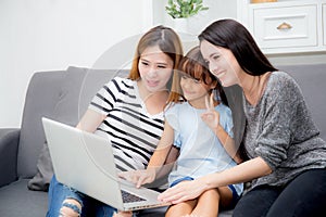 Mother, Aunt and kid having time together lerning with using laptop at home on couch photo
