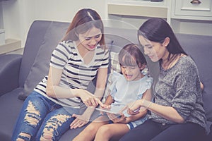 Mother, Aunt and kid having time together lerning with using tablet at home with relax and happy on couch