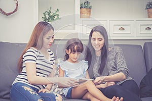 Mother, Aunt and kid having time together lerning with using tablet at home with relax and happy on couch