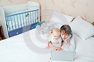 Mother with baby on the bed looking at a laptop with enthusiasm