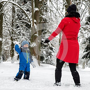 Mother with baby boy playing in snowy winter forest