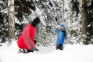 Mother with baby boy playing in snowy winter forest