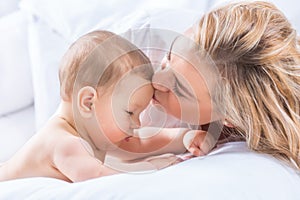 Mother and baby boy son playing on a white bed. Mothers tenderness and kisses of a toddler child