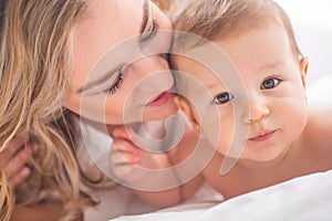 Mother and baby boy son playing on a white bed. Mothers tenderness and kisses of a toddler child