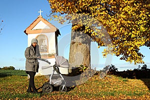 Mother with baby in carriage by chapel and tree