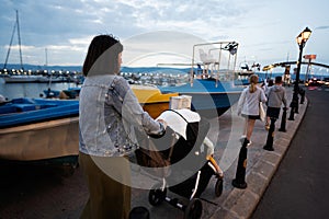 Mother with baby carriage on the pier in the evening, back view