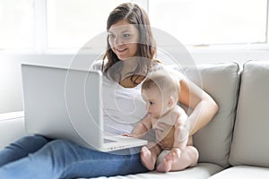 Mother and baby child are looking to play and read computer on the couch at home