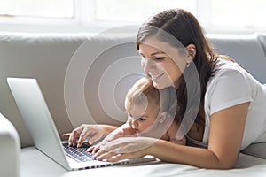 Mother and baby child are looking to play and read computer on the couch at home