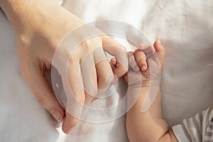 Mother Baby Connection. Newborn child holding mom& x27;s hand while lying in bed