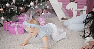 Mother with baby daughter crawling by Christmas tree