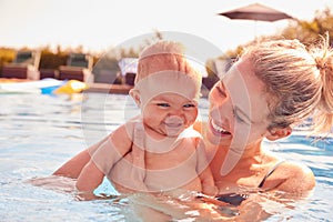 Mother With Baby Daughter Having Fun On Summer Vacation Splashing In Outdoor Swimming Pool