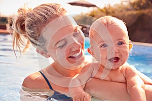 Mother With Baby Daughter Having Fun On Summer Vacation Splashing In Outdoor Swimming Pool