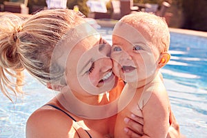 Mother With Baby Daughter Having Fun On Summer Vacation Splashing In Outdoor Swimming Pool