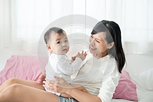 Mother and baby daughter plays, hugging, kissing at home on bed