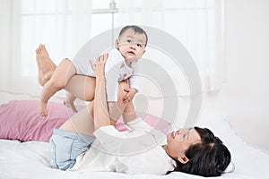 Mother and baby daughter plays, hugging, kissing at home on bed