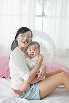 Mother and baby daughter plays, hugging, kissing at home on bed