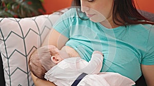 Mother and baby daughter sitting on sofa breastfeeding at home