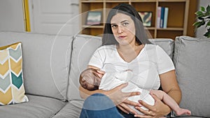 Mother and baby daughter sitting on sofa breastfeeding at home
