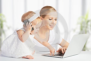 Mother with baby daughter works with a computer and phone