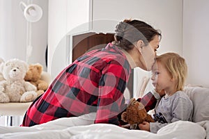 Mother and baby early in the morning, mom taking care of her sick boy. Baby in bed with fever and running nose