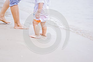 Mother and baby feet walking on sand beach.