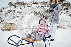 Mother and baby girl enjoy a sleigh ride. Child sledding. Kid riding a sledge on winter