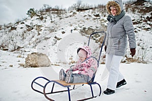 Mother and baby girl enjoy a sleigh ride. Child sledding. Kid riding a sledge on winter