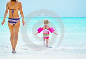 Mother and baby girl going into sea. rear view