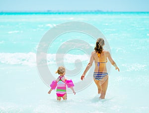 Mother and baby girl going into sea. rear view