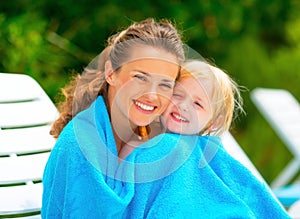 Mother and baby girl wrapped in towel on sunbed