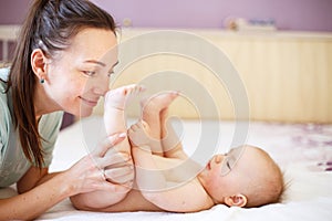 Mother and baby. Happy family. Mom`s love and tenderness. Mother massaging baby in the bed at home