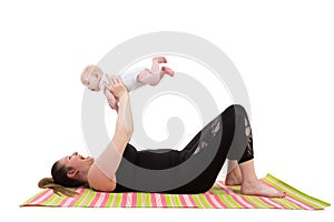 mother with baby having fun holding baby in the air while laying on a fitness mat