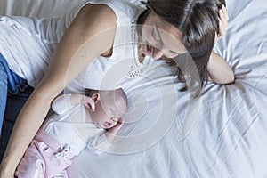 mother and baby at home lying on bed and relaxing. baby girl sleeping and mother looking at her. motherhood concept