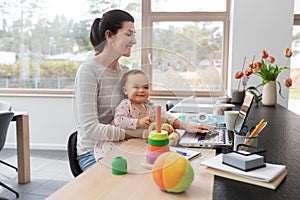 Mother with baby and laptop working at home office