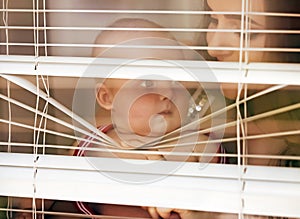 Mother with baby look through blinds. Woman and child at window shutters. Mothers day concept. Family love.