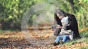 Mother with baby outdoor using mobile phone, autumn leaves background