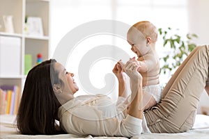 Mother and baby son playing in sunny bedroom. Parent and little kid relaxing at home. Family having fun together.