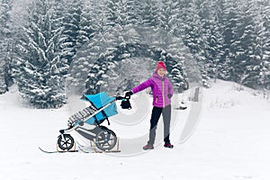 Mother with baby stroller enjoying motherhood in winter forest