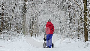 Mother with baby stroller enjoying motherhood in winter forest