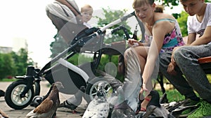 A mother with a baby in a stroller and an older son feeds pigeons with seeds.