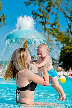 Mother and baby in swimming pool. Parent and child swim in a tropical resort. Summer outdoor activity for family with kids.